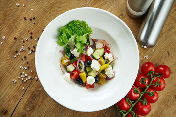 Classic Greek salad with tomatoes, onions, cucumber, feta cheese and black olives with olive oil on a white plate on a wooden background. Top view