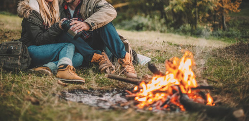 Traveler couple camping in the forest and relaxing near campfire after a hard day. Concept of trekking, adventure and seasonal vacation.