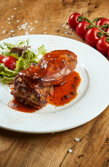 Close up view on roasted barbecue ribs in sweet and sour sauce with salad on a white plate on a wooden background