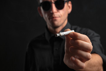 Close-up photo of a stylish young man in a black t-shirt and sun glasses showing cigarette