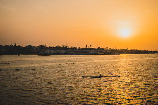 Sunset in Ziguinchor, Africa, observing it from the bridge over casamance river looking towards the ferry port. A fisherman with boat and nets are seen in the picture.