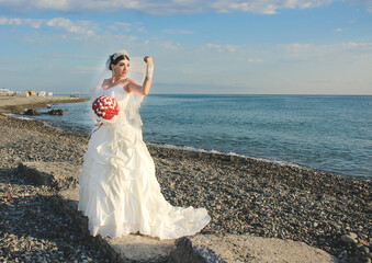 Fototapeta na wymiar Wedding by the sea. Beautiful bride with a red bouquet in a wedding dress at the water. Armenian bride on the stone beach in Batumi, Georgia. Concept marriage, just married 