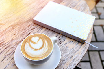 White cup of coffee and notebook close-up on a sunny day.