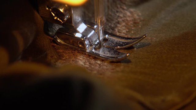 Close-up of the needle of a modern sewing machine darning khaki pants, it is close to each other doing stitches.