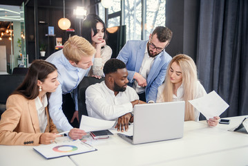 Multiethnic group young business colleagues having meeting about their business project and comparing data from different reports and table laptop.