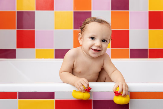 Smiling baby in bathtub holding rubber ducks