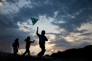 Children run with kite on summer sunset meadow silhouetted. playing outdoors.