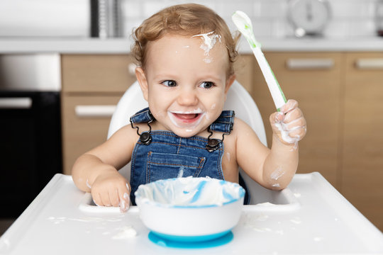 Happy baby with messy face eating yogurt with spoon