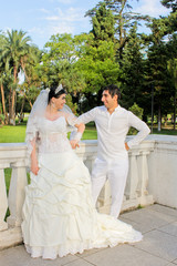 Funny couple of newlyweds. Bride with a red bouquet in a wedding dress at the palm trees on background. Happy wedding portrait. Concept marriage, just married, family, honeymoon.