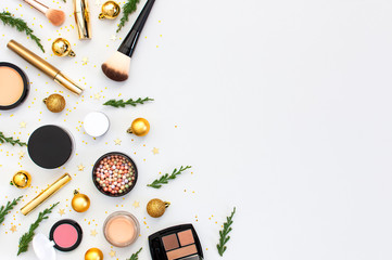 Makeup mascara foundation cream lipstick eyeshadow blush balls and New Year decorations gold Christmas balls confetti stars fir branches on light background Flat lay top view. Cosmetics, holiday Xmas