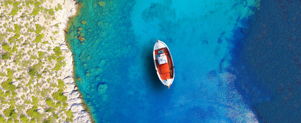 Aerial drone ultra wide photo of beautiful wooden traditional fishing boat docked in famous organised beach of Super Paradise, Mykonos island, Cyclades, Greece