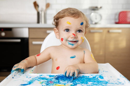 Baby sitting in high chair with finger paint on face and body