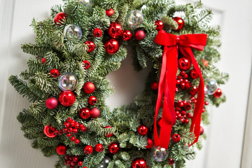 Fototapeta na wymiar Beautiful red Christmas wreath of fresh spruce on the white door. Entrance to the house. Christmas mood. Xmas tree.