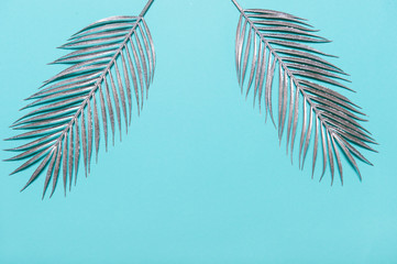 Border frame made of silver Tropical palm leaves on a blue pastel background