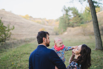 Young happy caucasian couple with little baby girl. Parents and daughter walking and having fun together. Mother and father play with child outdoors. Family, parenthood, childhood, happiness concept.