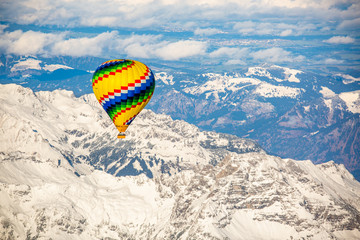 Luftaufnahme der schneebedeckten Alpen mit buntem Heißluftballon