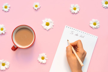 Flower composition with morning cup of coffee and a woman's hand holding pen and writing 'To do...