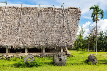 Traditional thatched yapese men's meeting house called faluw or fale and a bank of three historic megalithic stone money rai in front of it. A high coconut palm. Yap island, Micronesia, Oceania © Dmitry