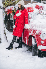 Young girl in a red coat near a red car with a Christmas tree on the roof. Christmas is comming. New Year.