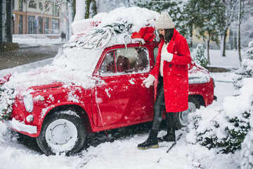 Young girl in a red coat near a red car with a Christmas tree on the roof. Christmas is comming. New Year.
