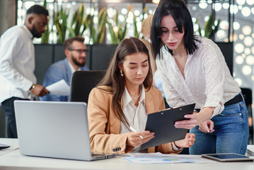 Attractive worker consulting with her office manager and signing financial document at her...