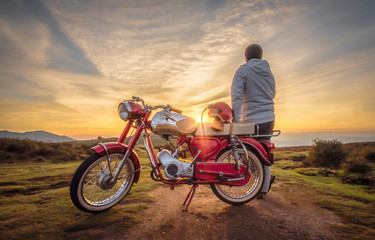 Fototapeta na wymiar Homem junto a moto antiga a ver o pôr do sol