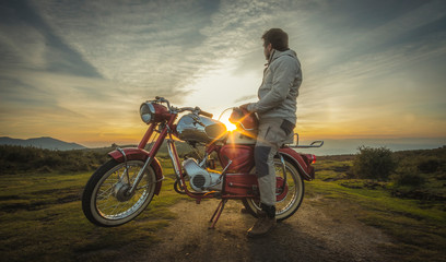Homem sentado na moto antiga a ver o pôr do sol