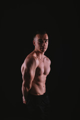 Fototapeta na wymiar Vertical portrait of muscular young man standing over dark background