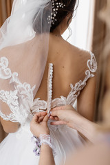 Obraz na płótnie Canvas Woman helps to fasten buttons on bride's wedding dress