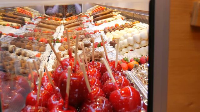 Various fruits on a wooden skewer stick in caramelized glaze made of milk black white chocolate. Apples in icing on the counter of the Christmas market. Street food