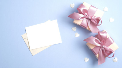 Happy Valentines day concept. Gift boxes with pink ribbon bow and romantic letter with blank postcard on pastel blue background with heart shaped confetti.
