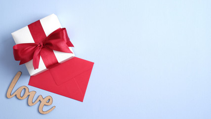 Happy Valentines Day concept. White gift box with red ribbon bow, red envelope, sign Love on pastel blue background. Flat lay, top view, copy space. Banner mockup for Valentines or Mothers Day