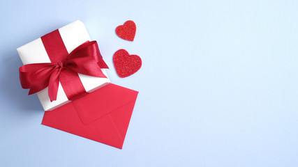 White gift box with red ribbon bow, red paper envelope and hearts on blue background. Flat lay, top view. Banner mockup for Saint Valentines day. Love and romance concept