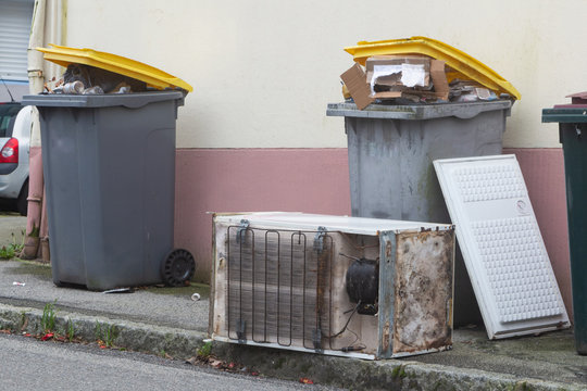 Full garbage bin and left-behind fridge in a street in Brest