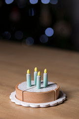 Toy birthday cake with candles on a wooden board on a dark spotlights background