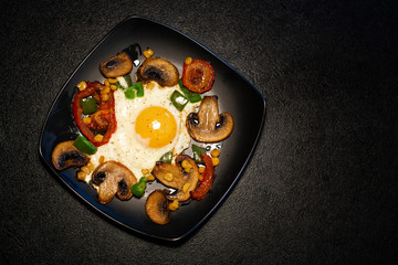 Freshly fried scrambled eggs with vegetables on a black plate