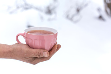 Hand holds a pink mug with a drink on a background of a winter landscape