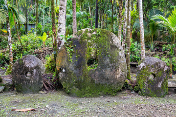 Three giant prehistoric megalithic stone coins or money Rai, under trees overgrown in jungle. Yap island, Federated States of Micronesia, Oceania, South Pacific Ocean