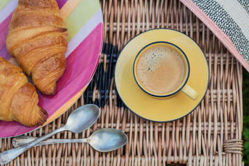 Two french croissants and cup of coffee on wicker basket.