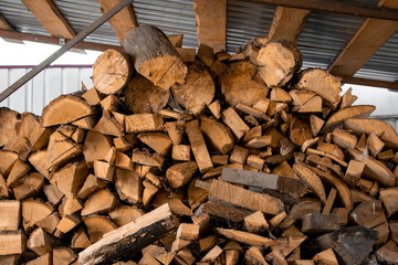 Pile of firewood under a canopy. Preparation of firewood for the winter. Heating season, eco-raw materials.