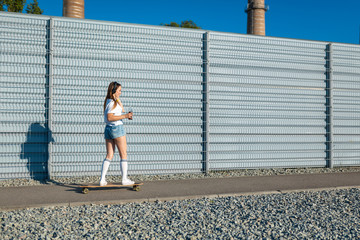 stylish girl in white stockings ride on longboard down the street and listening music. Space for text