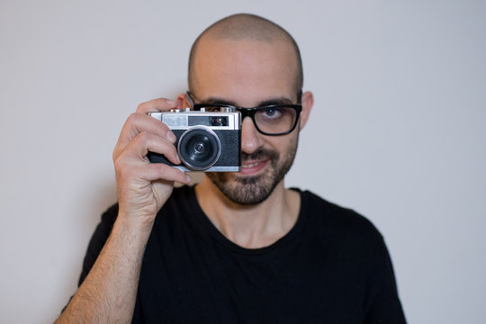 Caucasian smiling boy with beard takes a photo picture with a vintage retro 35mm film camera