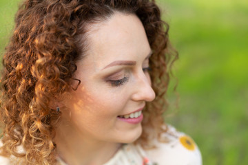 Close up portrait of young smiling attractive woman with curly hair in green flowering spring park. Pure emotions.