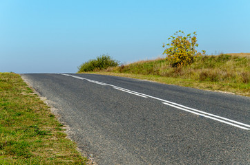 asphalt empty road and green grass. against the clear blue sky. autumn landscape
