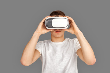 Freestyle. Young man in virtual reality headset standing isolated on grey watching video concentrated close-up