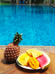 Fototapeta na wymiar Juicy tropical fruits set at pool edge with crystal blue water. Luxury weekend rest