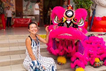 A European tourist girl at a Chinese New Year celebration in a Chinese temple is photographed with a traditional Chinese dragon. Festive Chinese entertainment