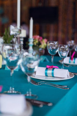 Table setting for a wedding party in pink and turquoise colors. Luxury decor. Plates, glasses, cutlery and candles. Vases with flowers.