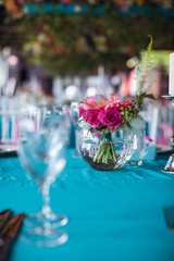 Table setting for a wedding party in pink and turquoise colors. Luxury decor. Plates, glasses, cutlery and candles. Vases with flowers.