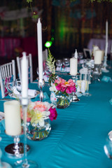 Table setting for a wedding party in pink and turquoise colors. White chairs with silk ribbons. Luxury decor. Plates, glasses, cutlery and candles. Vases with flowers.